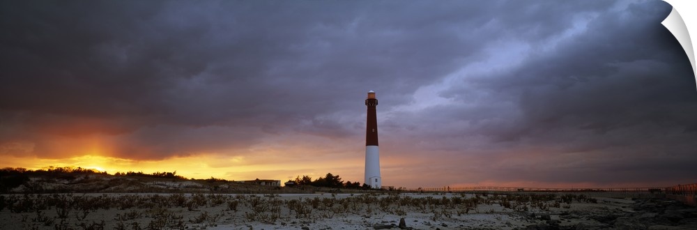 Panoramic photograph of watchtower on beach at dusk.  The sky is cloudy and the sun is barely visible.