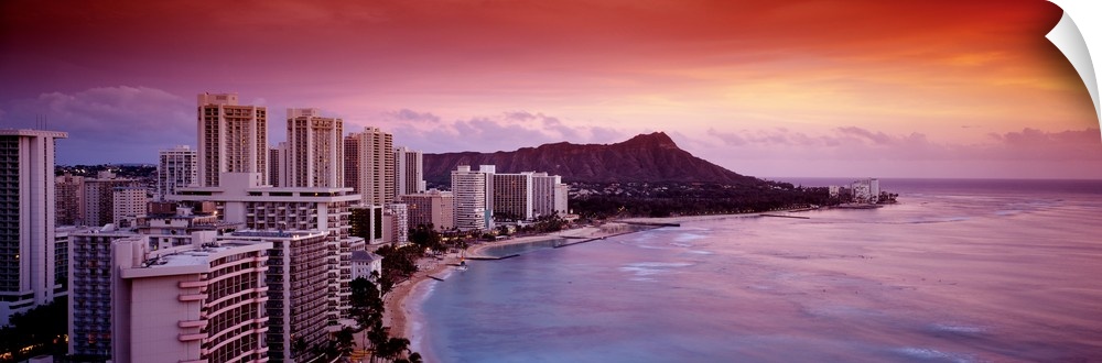 Rosy colors from the setting sun wash over the tropical island city next to the waterfront on Waikiki Beach, with Diamond ...