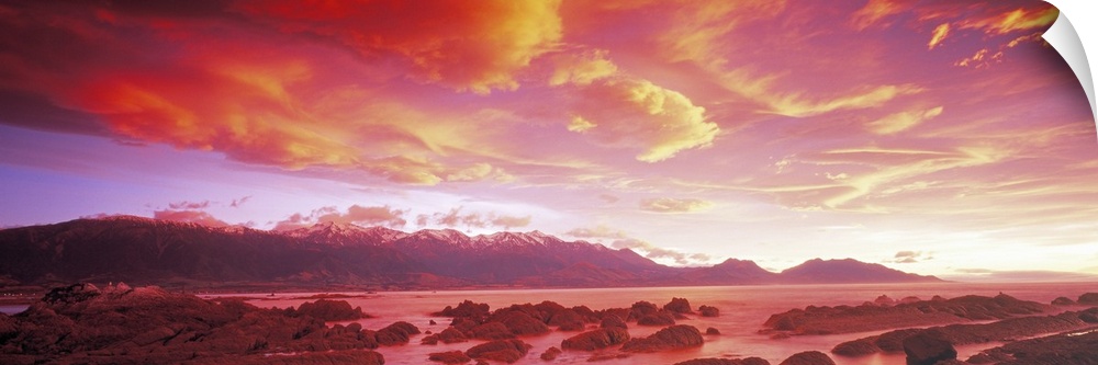 The sunset paints the sky with warm tones that hang over a mountain range and a body of water.