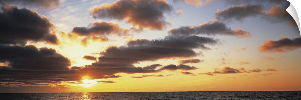Wide angle photograph of the sun setting slightly behind clouds, over the vast waters of Lake Michigan.