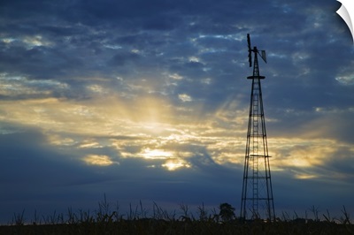 Sunset light through heavy clouds, silhouetted windmill, Iowa