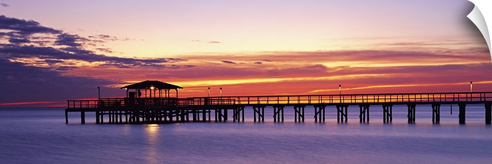 Wide angle photograph of Mobile Pier surrounded by deep purple waters beneath a vibrant sunset, in Mobile, Alabama.