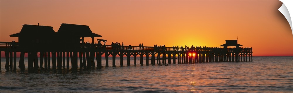 Panoramic canvas photo art of a silhouetted pier at sunset on the ocean.
