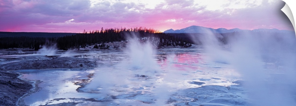 Large panoramic piece of geysers in Wyoming as the sun sets in the distance and gives the sky pink and purple hues.