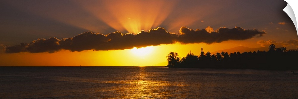Panoramic photograph of the sun setting behind the clouds over the water in Tahiti.