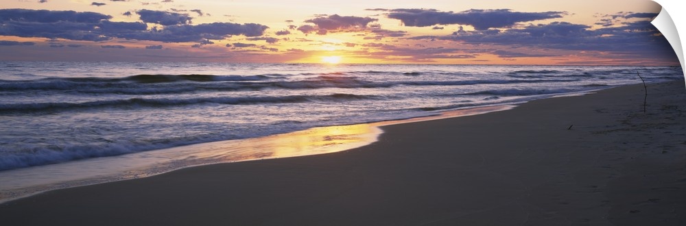 The sand and ocean are pictured in wide angle view with the sunset off in the distance.