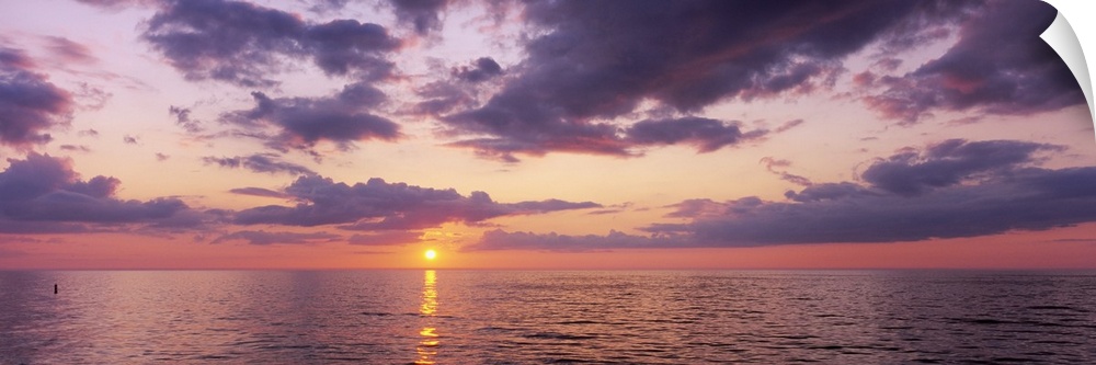Panoramic photograph taken of a sun setting over the Gulf of Mexico with warm colors throughout the sky.