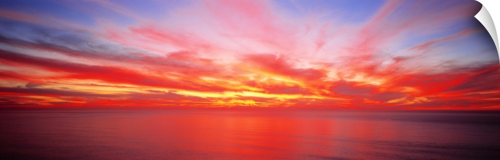 Wide angle photograph on a giant wall hanging of the sky full of streaking clouds during a vibrant sunset over the Pacific...