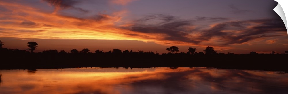 Panoramic photo on canvas of a bright sunset along a river in Africa with a tree line silhouetted against the sky.
