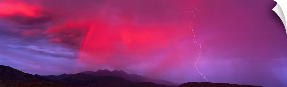 This panoramic photograph is taken of a sunset sky that is highlighted with hot pink and a bolt of lightning is striking d...