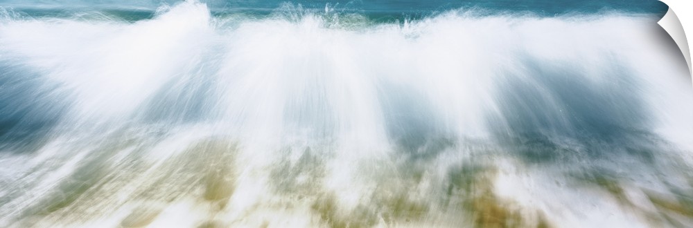 Up-close panoramic photograph of wave crashing onto beach creating spray.