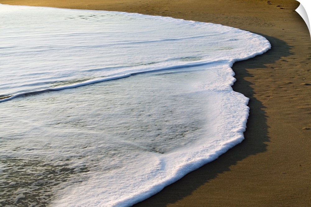 Horizontal, large photograph of the white surf covering part of the sand on a beach of the Outer Banks in North Carolina.