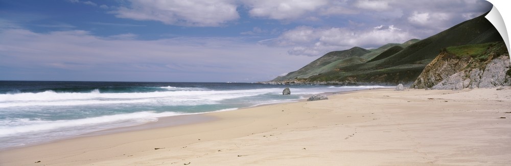 Panoramic photograph of shoreline with mountains.  There are waves rolling in under a cloudy sky.