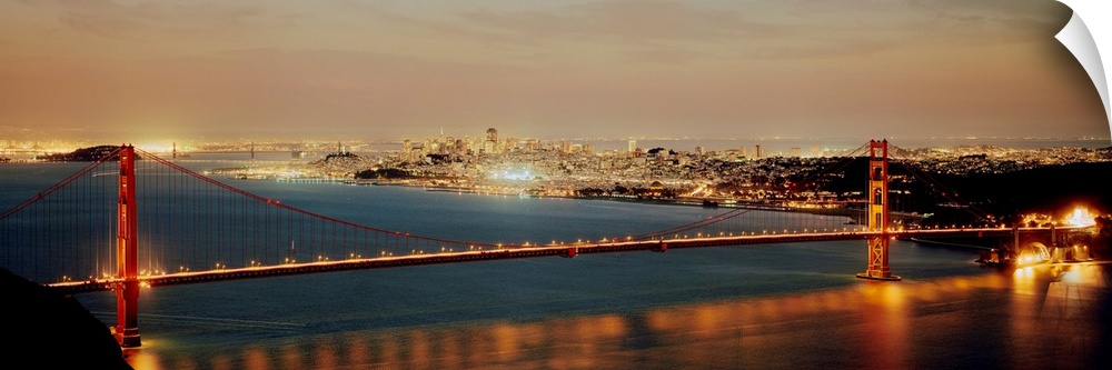 Panoramic photograph shows the bright lights of the Golden Gate bridge as they reflect onto the water below.  The vivid co...