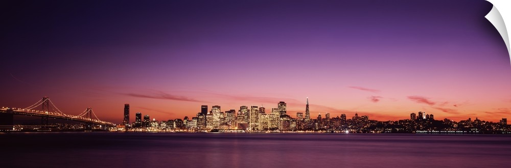 Dusk panoramic photo looking across the San Francisco Bay at the buildings lit up in downtown San Francisco and the Bay Br...