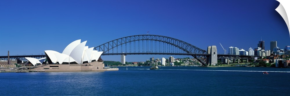 This is a panoramic photograph of the harbor with the suspension bridge, opera house, and city skyline in the background.