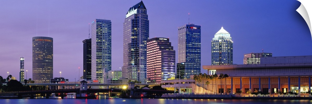 Wide angle photograph of the Tampa skyline in front a vivid sky, lit up at night and reflecting in the water.