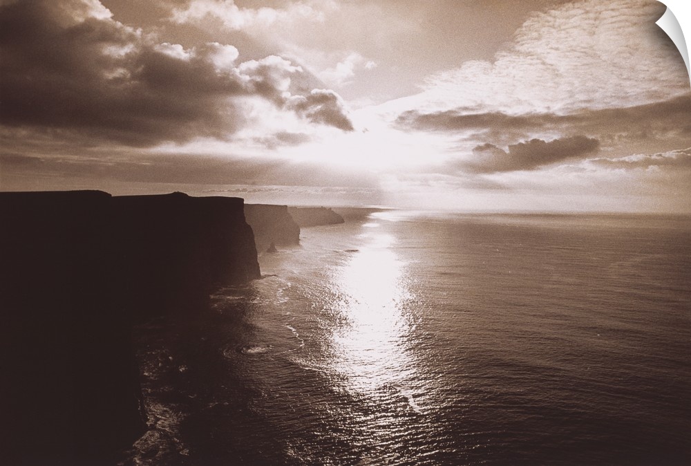 This big artwork piece is of a sepia toned sunset reflecting in the ocean water below with immense cliffs in Ireland pictu...
