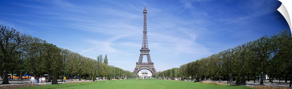 Tree lined grassy field in Paris with the Eiffel Tower protruding in to the clear blue sky.