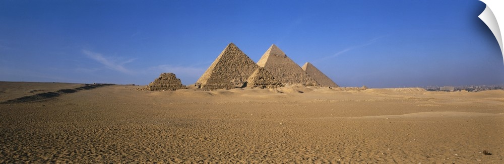 The pyramids in Egypt are photographed in wide angle view from a distance with a clear blue sky behind them.