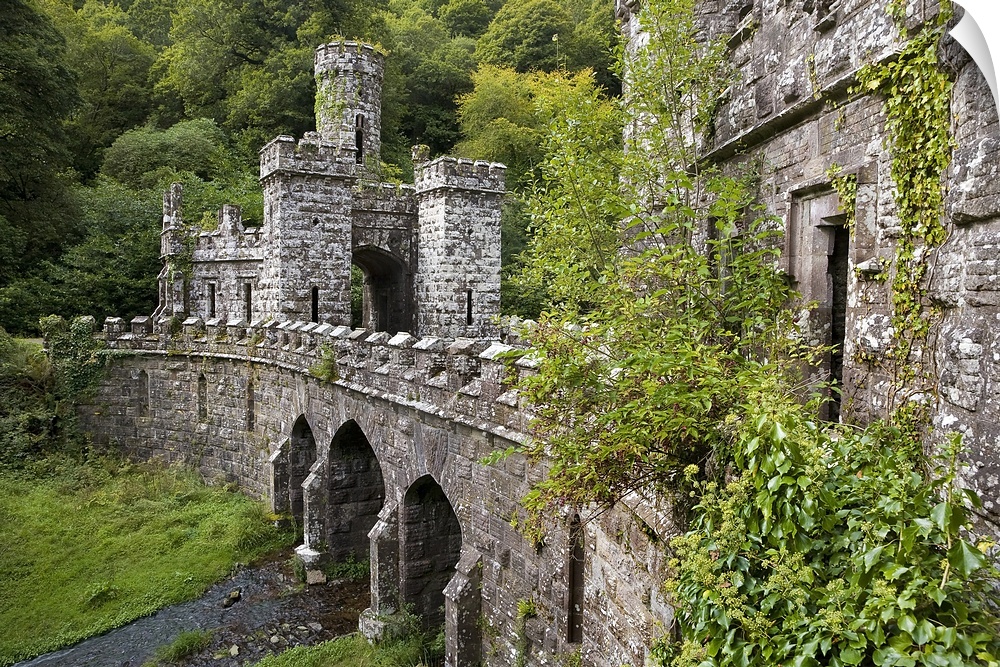 A side angle view of a large stone bridge and towers that are surrounded by greenery in Ireland.