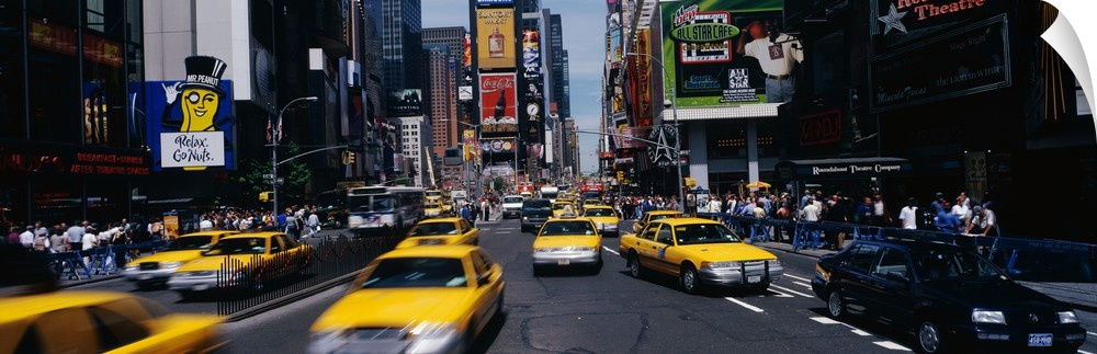 Wide angle photograph of many taxi cabs rushing through the streets, surrounded by the large advertising signs of Times Sq...