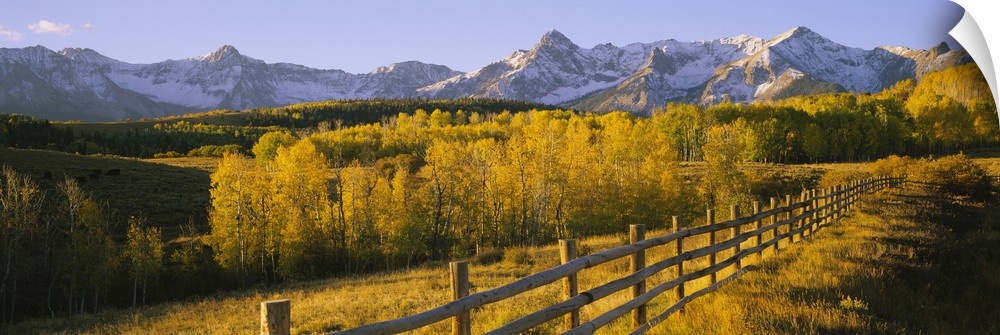 Panoramic view of the distant Rocky Mountains in the Midwestern United States, with a forest and a rustic fence in autumn.