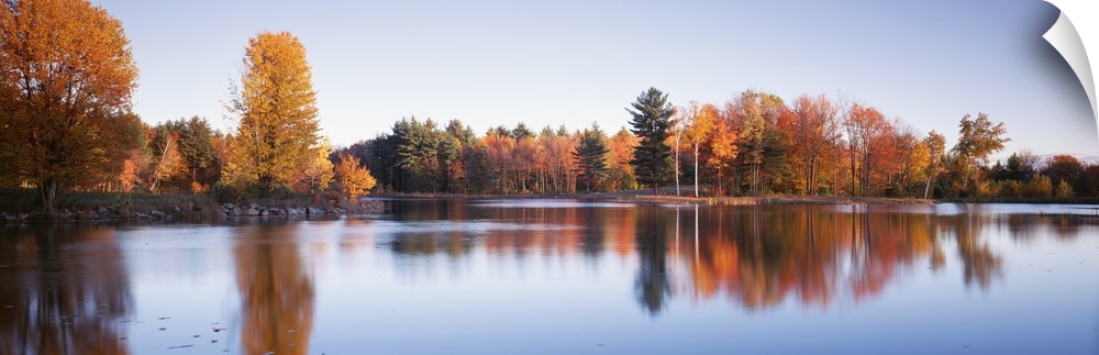 This photograph is taken behind a body of water of fall colored trees that line the other side of the lake.