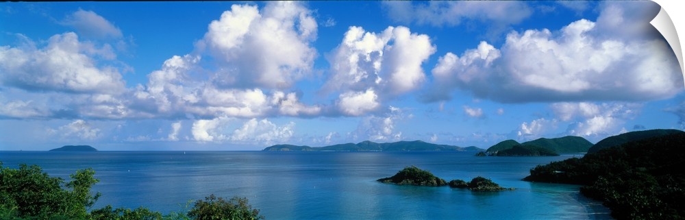 Panoramic photograph of ocean sprinkled with small grass covered islands under a cloudy sky.
