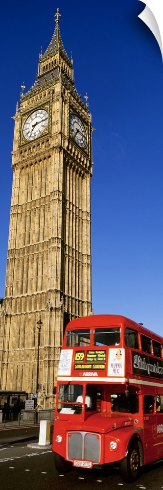 Vertical shot of Big Ben and a red London city bus driving by.