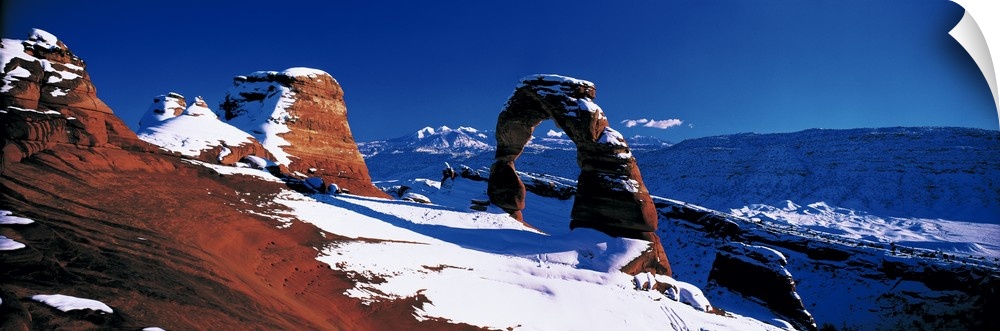 Snow covers desert land and stone arches that are photographed in panoramic view.