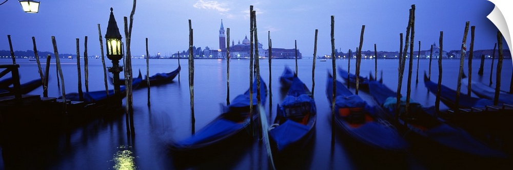 Line of gondolas moored against posts in the evening lit only by a single lamp and moonlight.