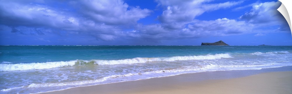 Panoramic photograph of waves breaking on the beach during a cloudy day with island in the distance .