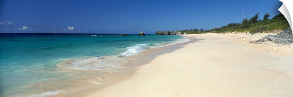 Ocean waves wash up on a sandy tropical shore in this panoramic seascape photographed on a sunny day.