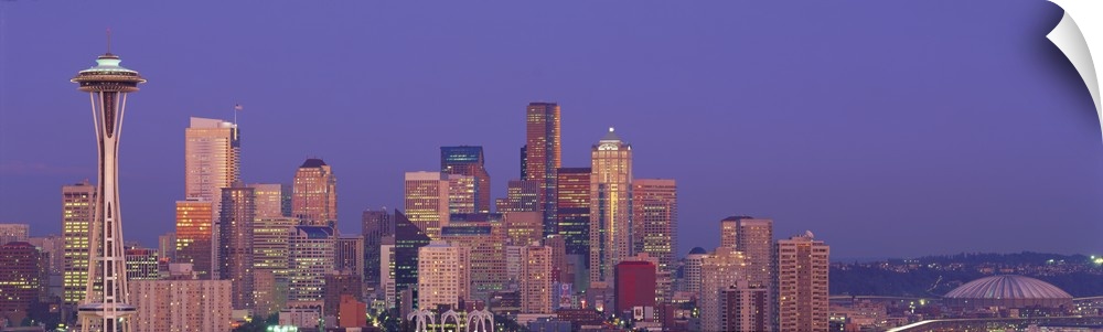 Panoramic photograph of lit up skyline at dusk with iconic buildings such as the Space Needle, Columbia Center, Smith Towe...