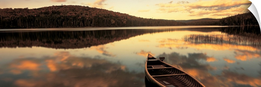 A canoe floats in a still lake at sunset in New England as clouds reflect in the water.