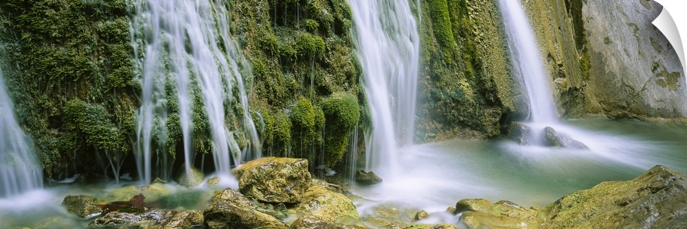 Panoramic photograph taken of several waterfalls cascading over foliage and crashing onto rocks.