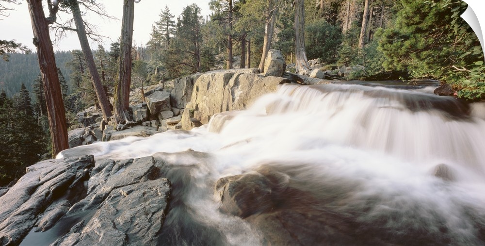A picture that has been taken of a waterfall flowing over large rocks and surrounded by a dense forest.