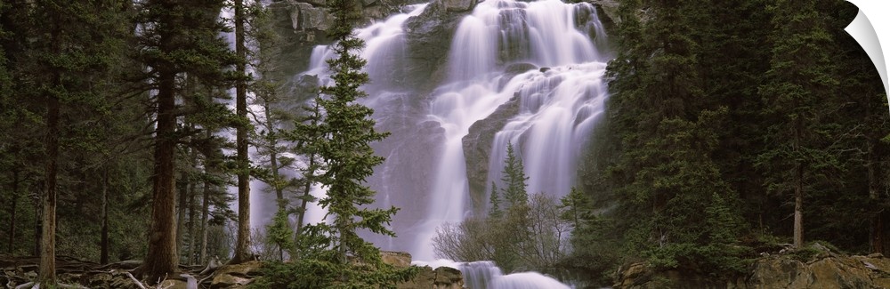 Panoramic photograph shows water furiously cascading down various steep rock faces within a dense woodland in North America.