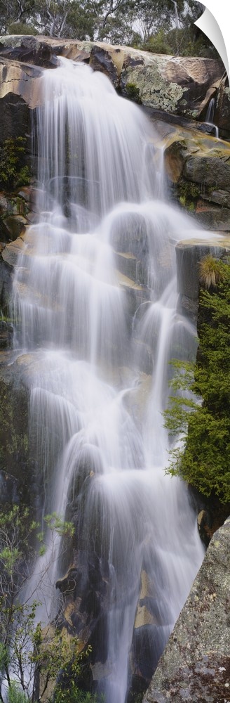 This tall waterfall is pictured in an elongated view as it flows over large rocks.