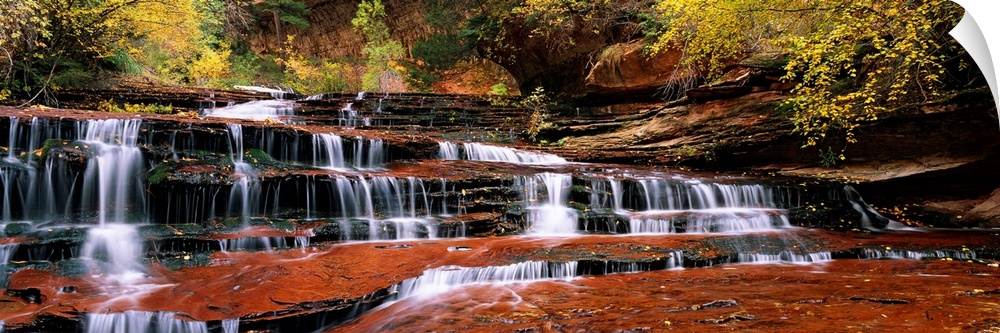 This panoramic photograph shows water trickling down the rock steps of a canyon waterfall.