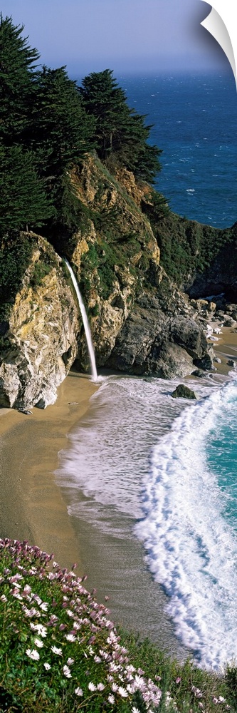 Vertical panoramic photo of a small waterfall in the rocky cliffs of the Pacific coast at low tide.