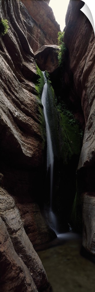 Vertical panoramic photograph of cascading water falling between tall rock formations.