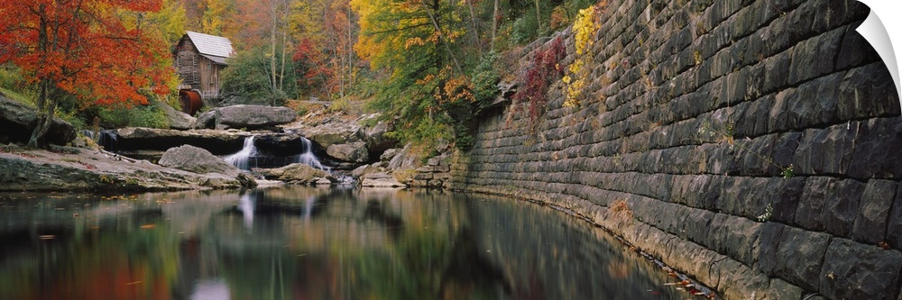 Panoramic photo of a lake with a mill in the distance surrounded by fall foliage.