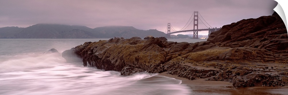 Panoramic photograph shows waves breaking against the rocky shores of Baker Beach in San Francisco, California.  In the ba...