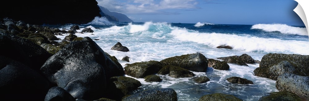 Panoramic photograph on a big canvas of waves crashing onto large rocks along the coast of Na Pali in Kauai, Hawaii.