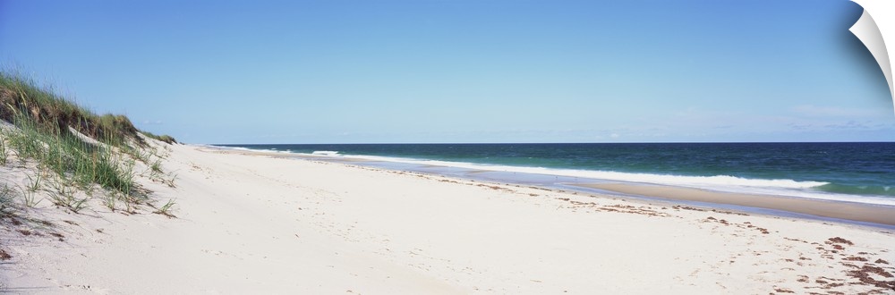 Panoramic photograph taken of the beach with the sand dunes just to the left and the ocean water coming up onto the sand.
