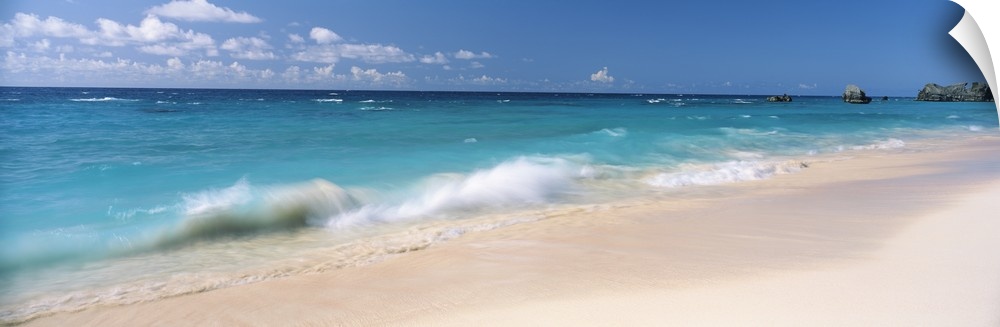 Tropical scene of clear turquoise ocean waves splashing on the sandy beach in the Caribbean, some boats in the distance.