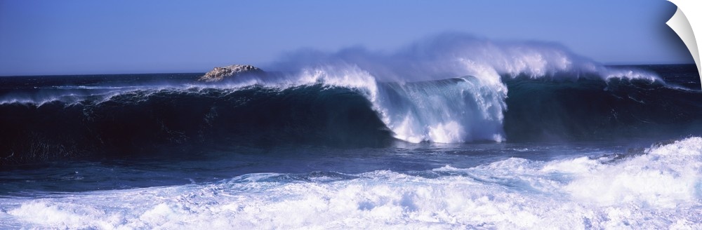 This panoramic beach photograph captures a wave curling and breaking off the shore.
