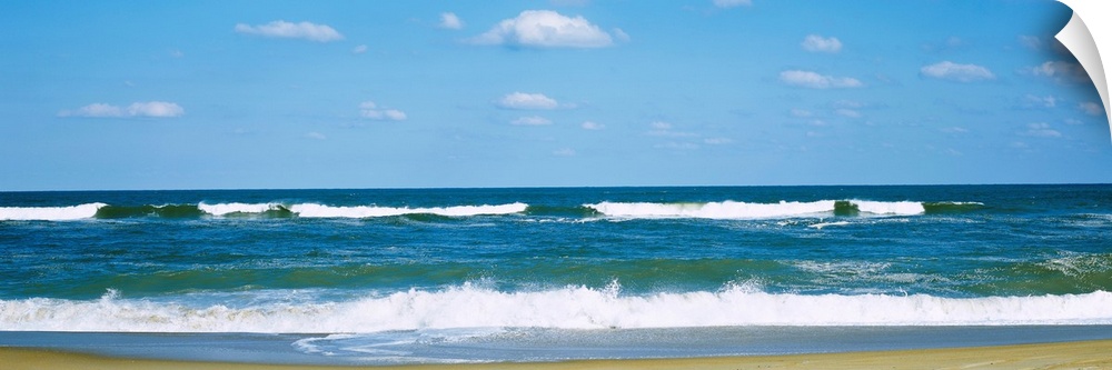 Panoramic landscape photograph of a clear day at the beach with waves washing up on the sandy beach.